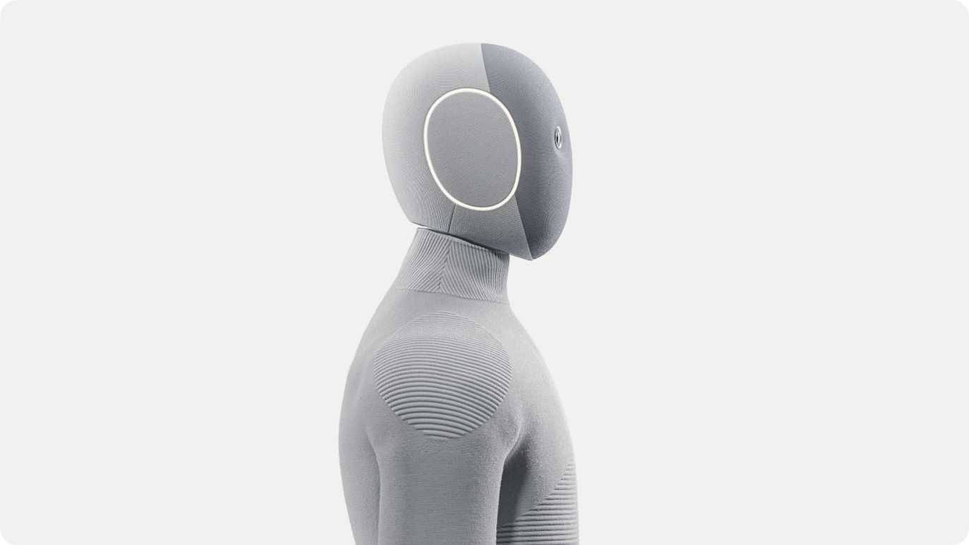 Close side view of a humanoid robot's head and shoulders in light-gray ribbed knit, with a circular ring on the face.