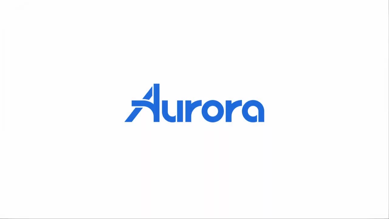 Aurora Driver autonomous freight truck, a dark tractor unit with roof- and bumper-mounted sensor pods, hauling a white trailer on a highway.