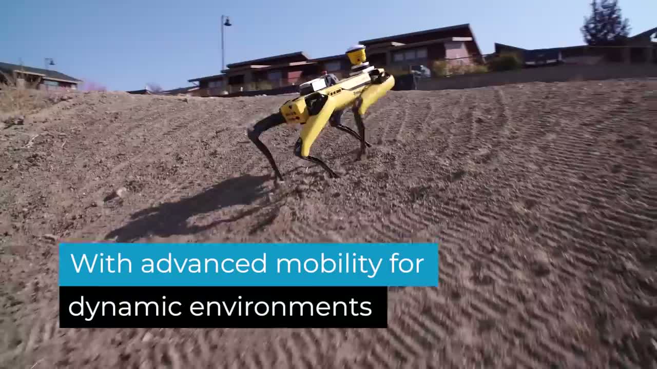 Boston Dynamics Spot, a yellow-and-black quadruped robot with a sensor mast, walking across a graded dirt slope at a construction site. The source video overlays the text "With advanced mobility for dynamic environments".