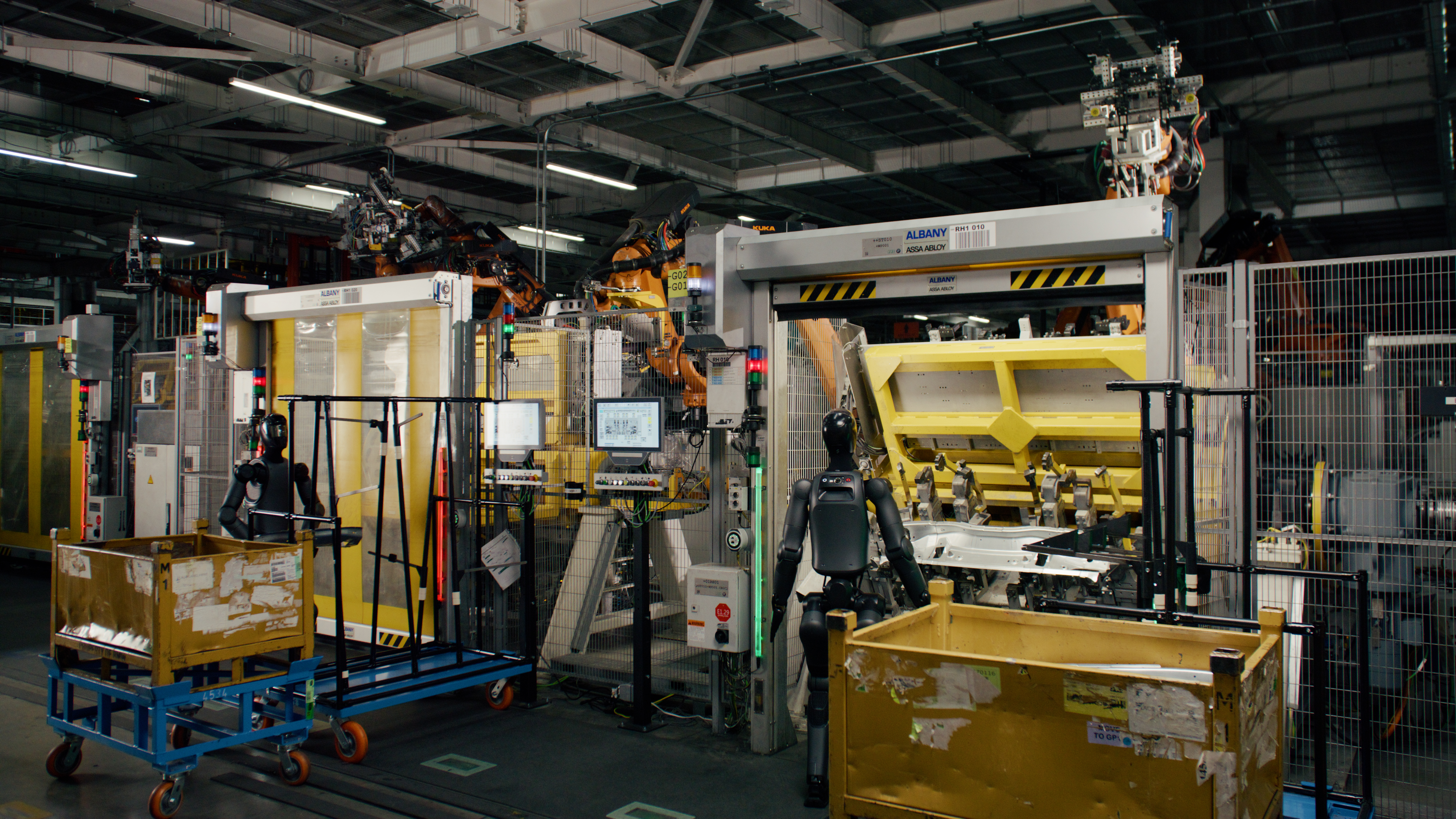 Two black Figure 02 humanoid robots on an automotive body-shop line beside parts carts and industrial robots.