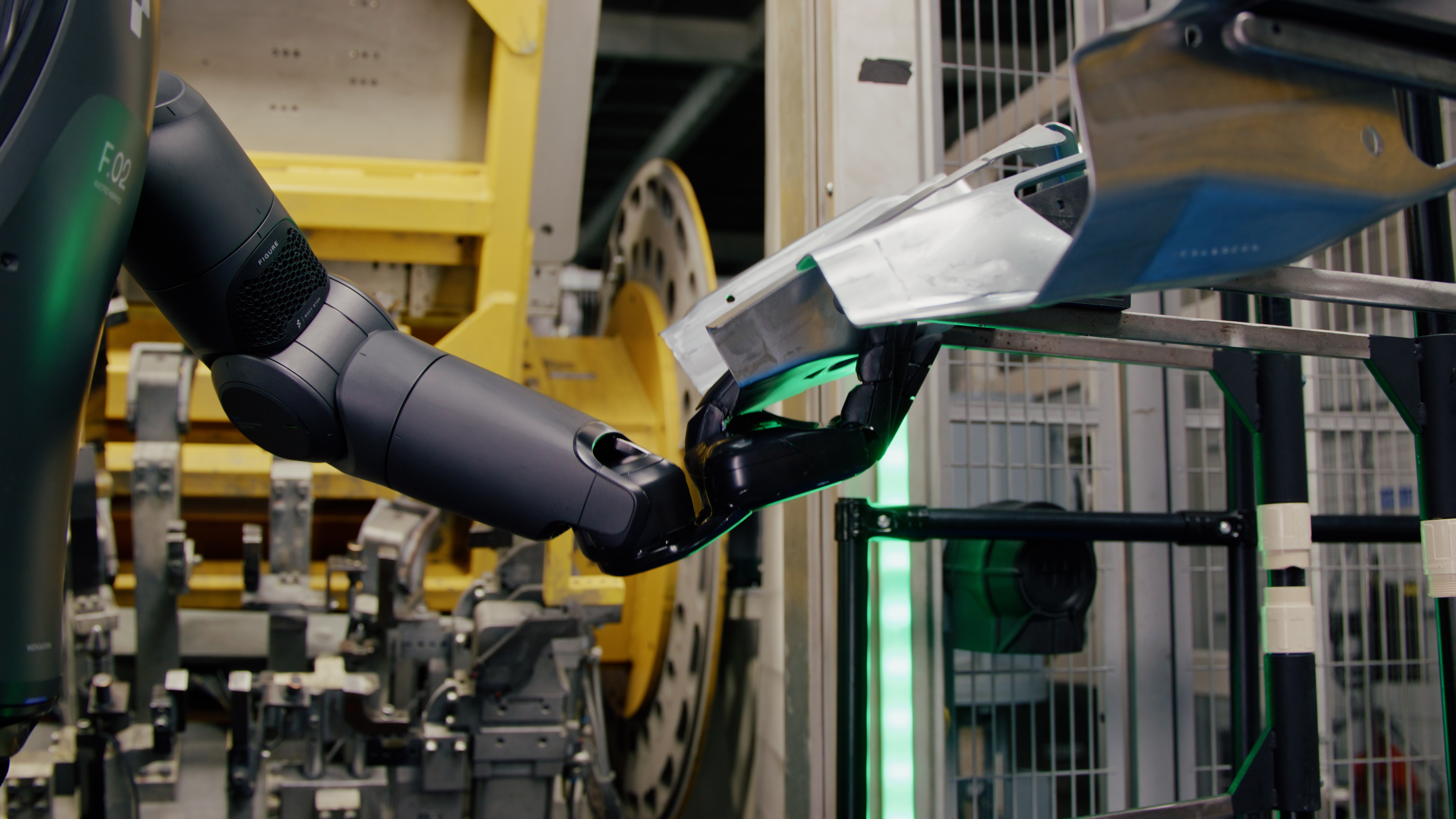 A black Figure 02 robot arm gripping a metallic sheet-metal car-body panel on an automotive production line.