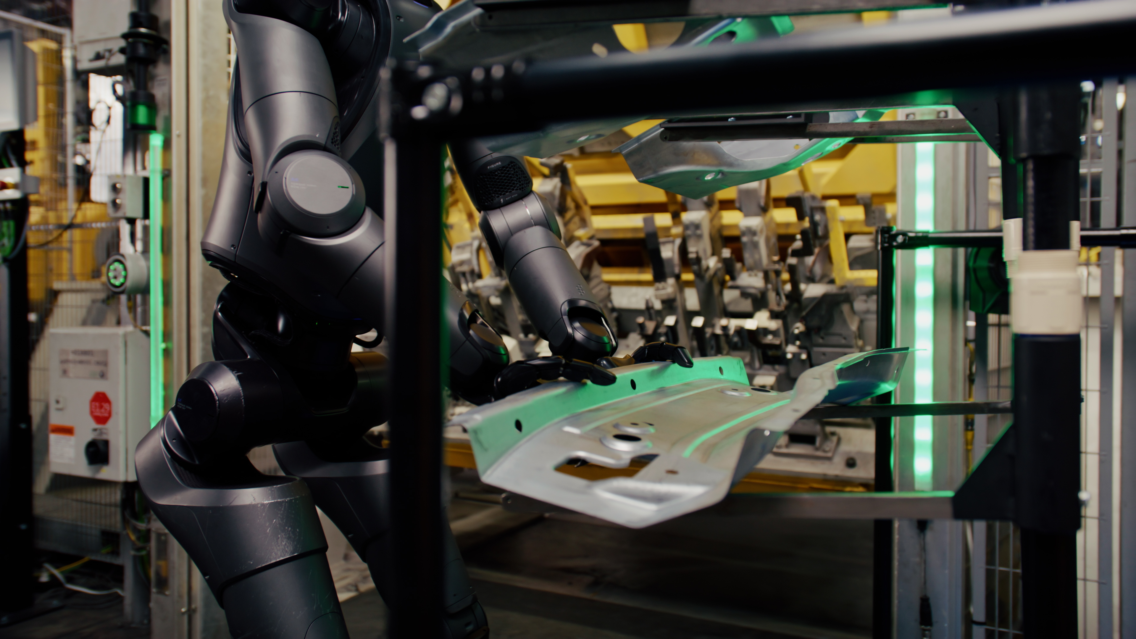 A black Figure 02 robot arm reaching down to a sheet-metal car-body part on a fixture under green scanning light.