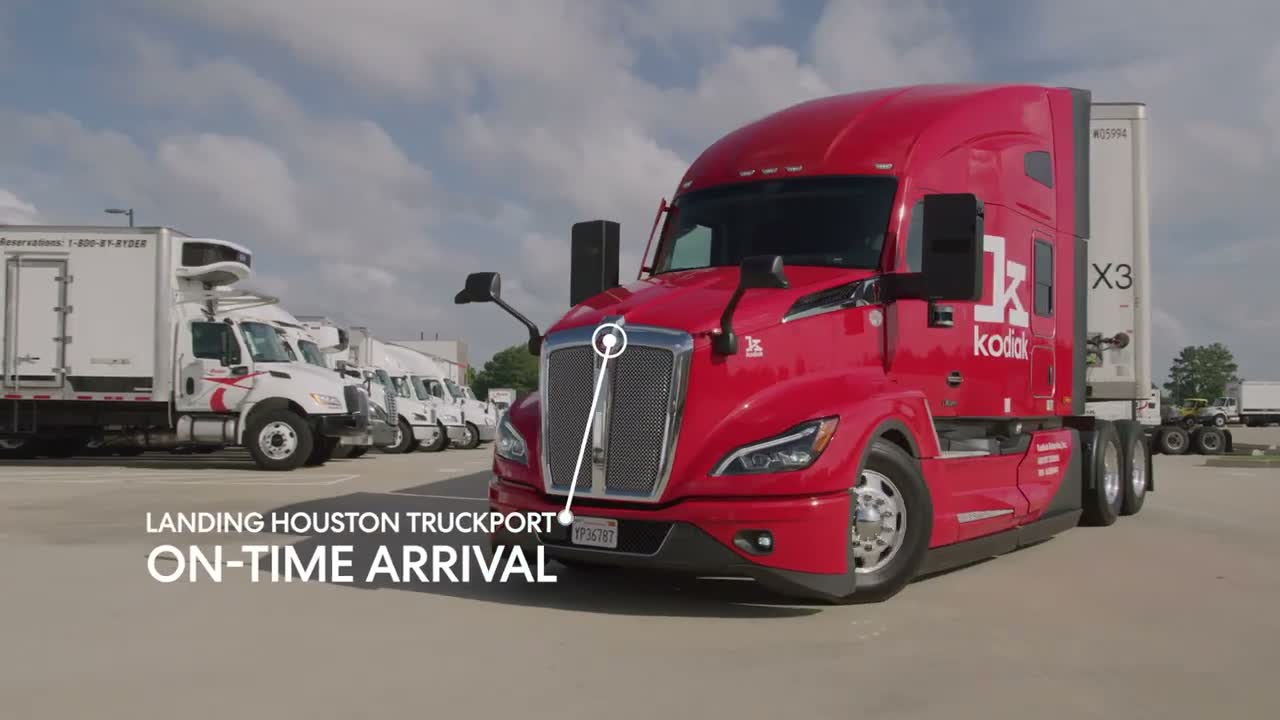 Kodiak Driver autonomous freight truck, a red tractor unit with "kodiak" branding and roof- and side-mounted sensor pods, parked at a truck yard. The source video overlays the on-screen text "Landing Houston Truckport" and "On-Time Arrival".